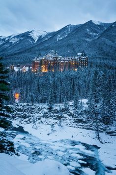 a large building in the middle of a snowy forest with trees and mountains behind it