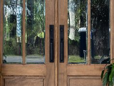 two wooden doors with glass on them in front of some trees and bushes, one has a black door handle