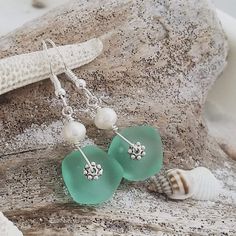 sea glass and pearl earrings are displayed on a rock next to a starfish shell