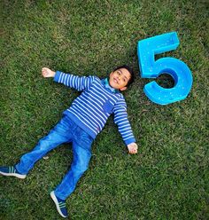 a young boy laying on the grass next to a number five