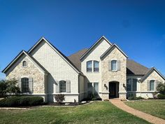 a large white brick house in the middle of a grassy area with trees and bushes