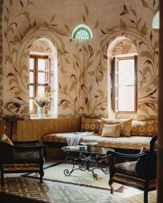 a living room filled with lots of furniture and windows covered in floral wall coverings