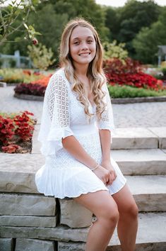 a young woman sitting on steps in front of flowers and trees, smiling at the camera