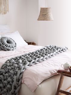 a bed with a blanket on top of it next to a table and lamp hanging from the ceiling