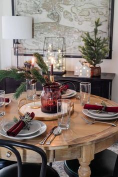 a dining room table set for christmas with candles and greenery on the centerpiece