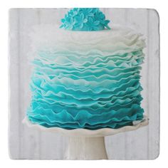 a blue and white cake with ruffles on the top is sitting on a pedestal