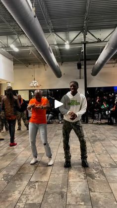 two young men are dancing on the dance floor in an indoor area with people watching