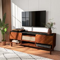 a living room with a large television on top of a wooden entertainment center next to a potted plant