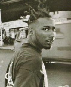 a black and white photo of a man with dreadlocks walking down the street