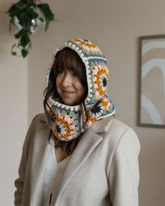 a woman wearing a crocheted hoodie and jacket in front of a plant