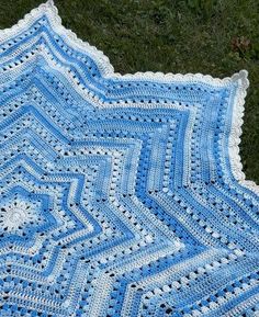 a blue and white crocheted blanket laying on the grass