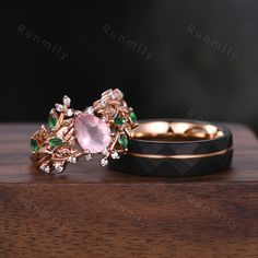 two gold rings with green and pink stones on top of each other, sitting on a wooden surface