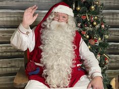 a man dressed as santa claus sitting in front of a christmas tree with his hands up