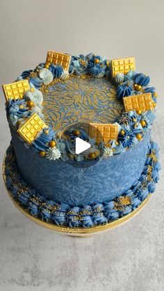 a blue and yellow cake with gold decorations on the top is sitting on a table