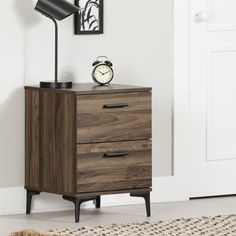 a night stand with two drawers and a clock on it in front of a door