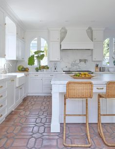 two wicker chairs sit in front of a white kitchen island with marble counter tops