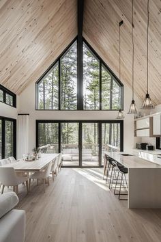 a large open concept kitchen and dining room with wood ceilinging, white furniture and windows