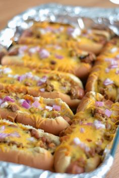 several hot dogs with cheese and onions in a tin pan on a wooden table top