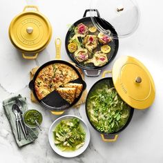 four pans with different types of food in them on a marble counter top next to plates and utensils