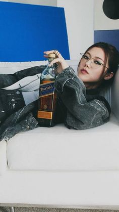 a woman sitting on a couch with a bottle of liquor in her hand and looking at the camera