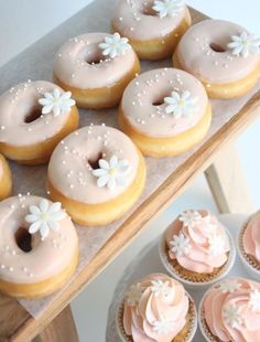 there are many pink frosted donuts on the tray and cupcakes next to them