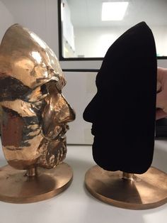 two gold head sculptures sitting on top of each other in front of a white wall