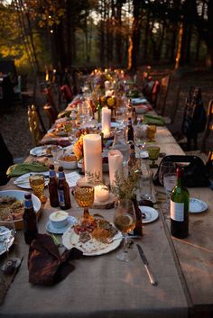 a long table is set up with candles and plates for an outdoor dinner party in the woods