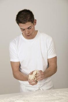 a young man holding a teddy bear in front of a white wall and looking down at it