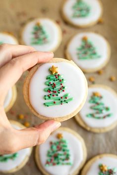 a person holding a decorated christmas tree cookie in front of some cookies on a table