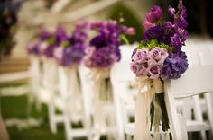 rows of white chairs with purple flowers tied to the back and sides, all lined up