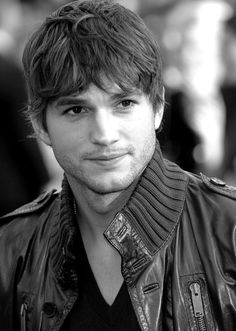 a young man wearing a leather jacket and looking at the camera while standing in front of a crowd