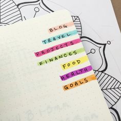 an open notebook with colorful sticky notes on the pages that read blog travel projects finance food health goals