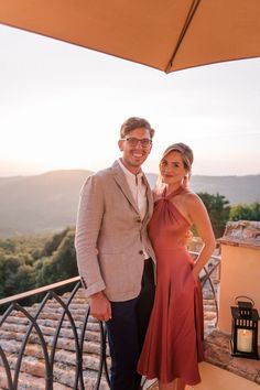 a man and woman posing for a photo on a balcony overlooking the mountains at sunset