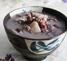 a bowl of soup with beans and meat in it next to a flower on the table