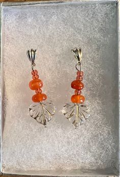 Amber brightens and welcomes the golden hues of fall! These earrings hold chunks of polished amber with tiny pale orange-pink glass seed beads, and clear gold embossed glass leaves, hung from silver posts. Orange Czech Glass Dangle Earrings, Amber Czech Glass Dangle Earrings, Handmade Amber Earrings In Czech Glass, Amber Czech Glass Earrings With Ear Wire, Handmade Orange Carnelian Earrings, Handmade Carnelian Orange Earrings, Nickel Free Carnelian Orange Earrings, Nickel-free Amber Czech Glass Earrings, Orange Carnelian Dangle Earrings