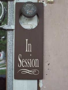 a sign that says in session hanging on the side of a building with a door handle