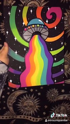 someone is holding up a painting with a space ship in the center and rainbows on it