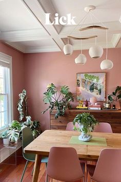 a dining room with pink walls and wooden table surrounded by potted plants on the wall