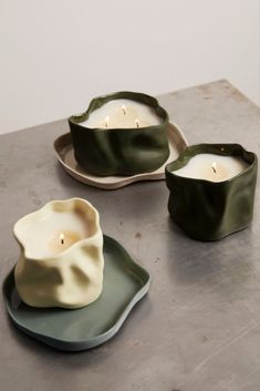 two green and white dishes with candles in them sitting on a gray table top next to each other