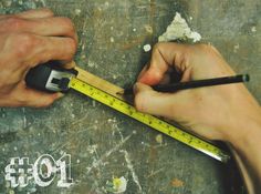 two hands holding a tape measure and a pair of scissors on top of a piece of wood