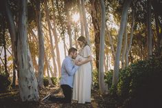 a man kneeling down next to a woman in front of trees