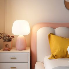 a white bed with two nightstands and a pink lamp on the night stand next to it