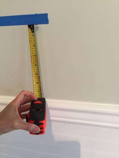 a hand holding a tape measure in front of a wall with blue tape on it