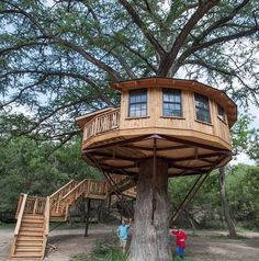 two people standing in front of a tree house with stairs leading up to the top