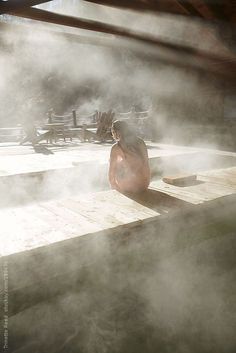 a person sitting on a wooden platform in the middle of steam rising from it's surface