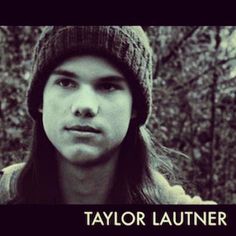 a young man with long hair wearing a beanie and looking at the camera in front of trees