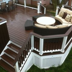 a deck with chairs and tables on it next to a house in the grass,