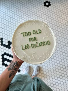 a person holding up a cake that says too old for leo dicaprio on it