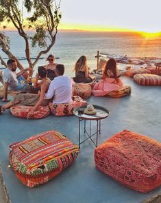 a group of people sitting on bean bags in front of the ocean at sunset or sunrise