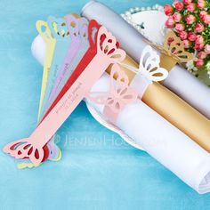 three different colored paper butterflies on a white plate next to flowers and a vase with pink roses